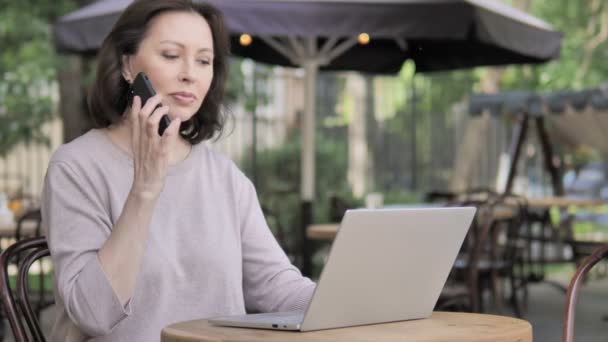 Mulher velha falando no telefone, sentado no café ao ar livre — Vídeo de Stock