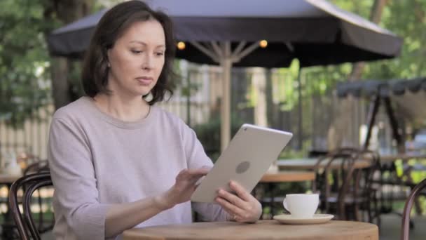 Старуха празднует победу на планшете в открытом кафе — стоковое видео