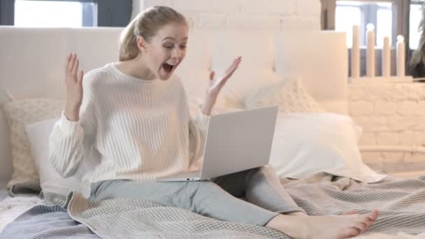 Молодая женщина празднует успех на ноутбуке, сидя в постели — стоковое видео