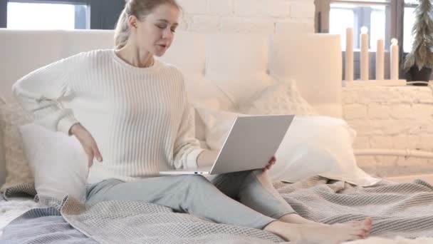 Jonge vrouw met rugpijn werken op laptop in bed — Stockvideo