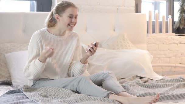 Восхитительная женщина сидит в постели и празднует успех на смартфоне — стоковое видео