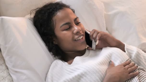 Bovenaanzicht van jonge Afrikaanse vrouw praten op de telefoon in bed — Stockvideo