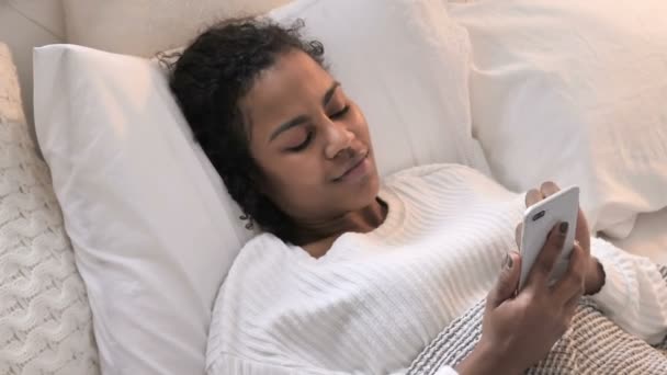 Top uitzicht van Afrikaanse vrouw met behulp van smartphone terwijl ontspannen in bed — Stockvideo