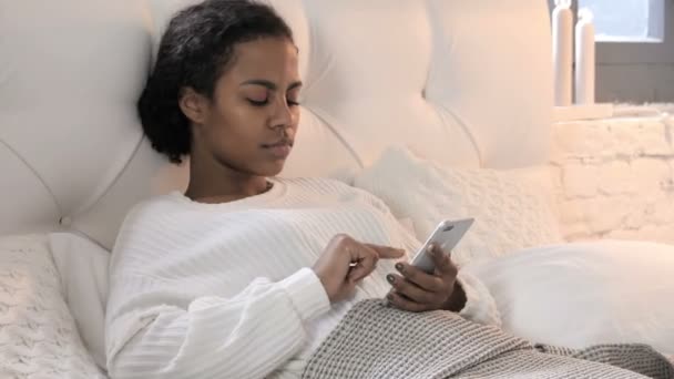 Giovane donna africana utilizzando smartphone mentre si rilassa a letto — Video Stock