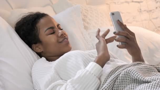 Jonge Afrikaanse vrouw met behulp van smartphone terwijl het leggen in bed — Stockvideo