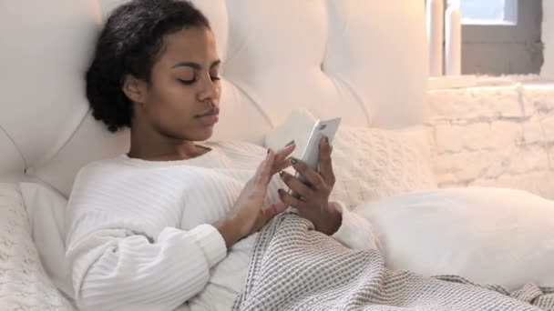 年轻的非洲妇女庆祝成功，同时使用智能手机在床上 — 图库视频影像