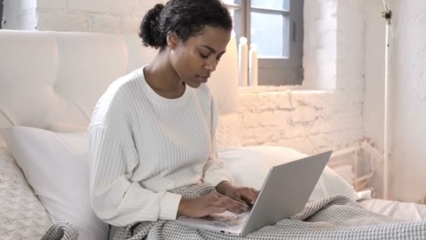 Mujer joven africana sentada en la cama y trabajando en el ordenador portátil — Vídeos de Stock