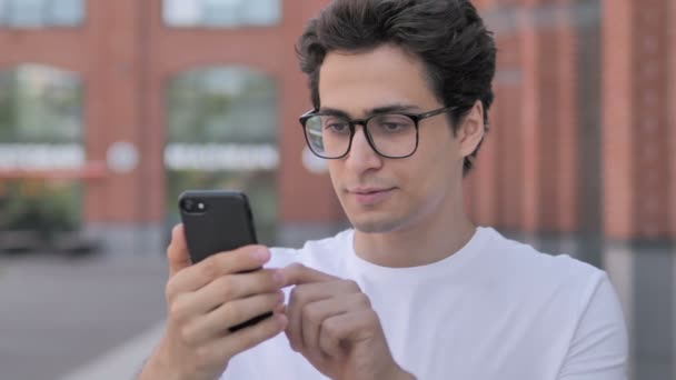 Retrato al aire libre del joven que anima el éxito en el teléfono inteligente — Vídeos de Stock