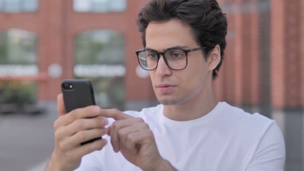 Retrato al aire libre de hombre joven molesto por la pérdida en el teléfono inteligente — Vídeos de Stock