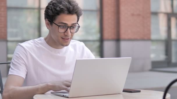 Jeune homme célébrant le succès sur ordinateur portable, assis en plein air — Video