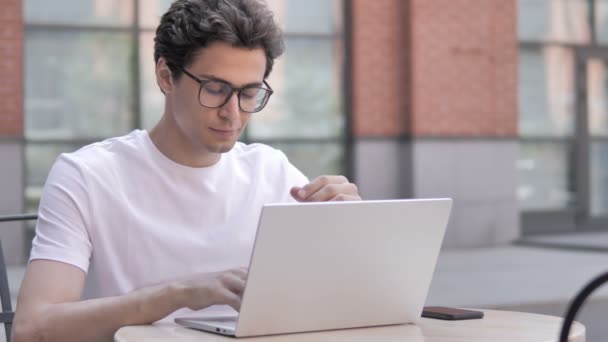 Ung man med huvudvärk arbetar på laptop, sittande utomhus — Stockvideo