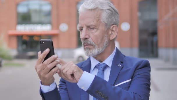 Retrato al aire libre del viejo empresario molesto por la pérdida en el teléfono inteligente — Vídeos de Stock