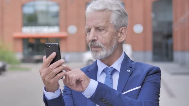 Retrato al aire libre del viejo empresario animando el éxito en el teléfono inteligente — Vídeo de stock