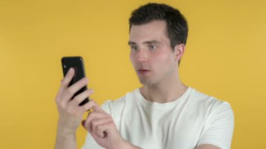 Kayıp tepki genç adam ve Sarı Arka Plan izole Smartphone kullanma