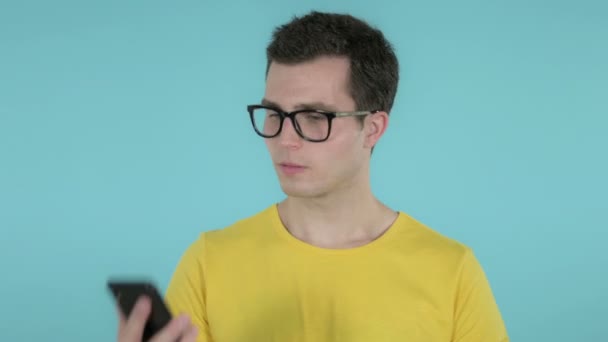 Молодий чоловік говорить на смартфоні, ізольованому на синьому фоні. — стокове відео