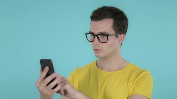 블루 배경에 고립 된 스마트 폰을 검색 하는 젊은 남자 — 비디오