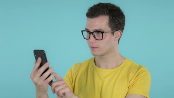 Jonge man enthousiast voor succes tijdens het gebruik van smartphone geïsoleerd op blauwe achtergrond — Stockvideo