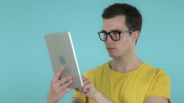 Hombre joven navegando internamente en la tableta, fondo azul — Vídeo de stock