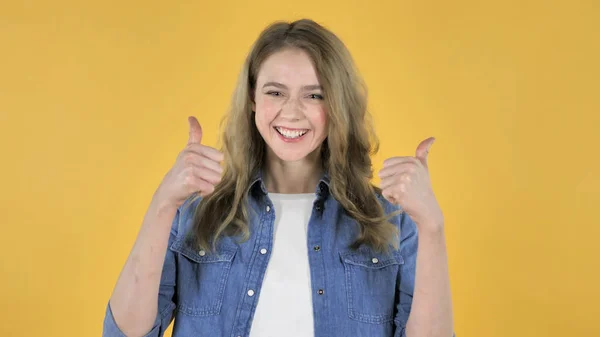 Jovem menina bonita Gesturing Polegares para cima no fundo amarelo — Fotografia de Stock