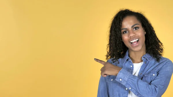 African Girl Pointing with Finger on Side, Yellow Background