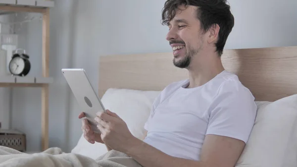 Онлайн видео чат на планшете молодого человека в постели — стоковое фото