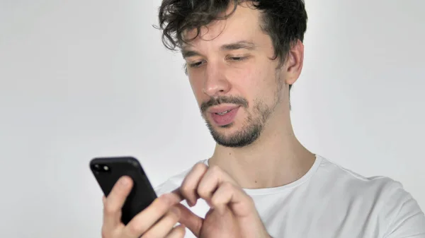 Молодой случайный человек просматривает смартфон, белый фон — стоковое фото