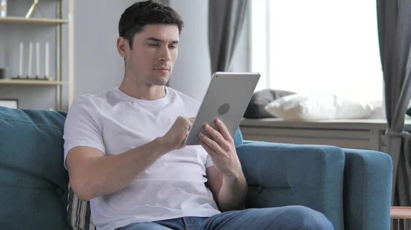 Mladý muž používání tabletu při relaxaci na gauči — Stock fotografie