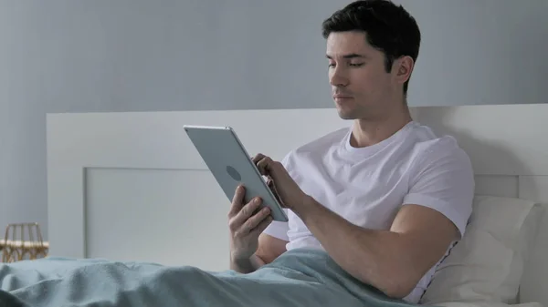 Молодой человек просматривает Интернет на планшете в постели — стоковое фото