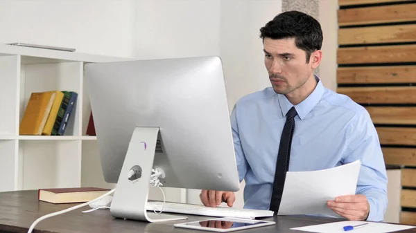 Papeleo, Joven Empresario leyendo documentos y trabajando en la computadora — Foto de Stock