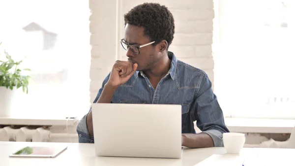 Hombre africano creativo enfermo tosiendo y trabajando en el ordenador portátil —  Fotos de Stock