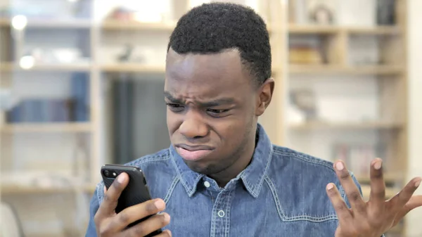 Hombre joven africano reaccionando a la pérdida en el teléfono inteligente —  Fotos de Stock