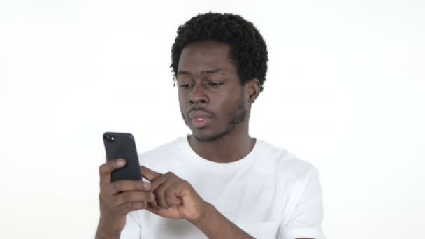 Ung afrikansk man reagerar på förlust och använda smartphone isolerad på vit bakgrund — Stockvideo