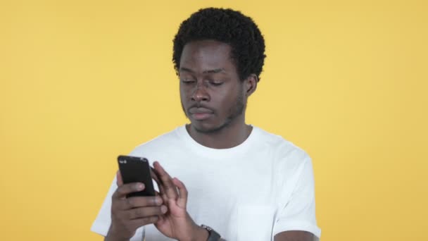 Joven africano emocionado por el éxito mientras usa Smartphone aislado sobre fondo amarillo — Vídeos de Stock