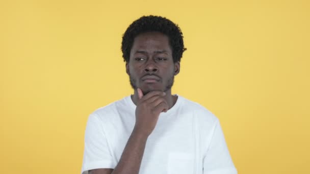 Pensando que el joven africano tiene una nueva idea aislada en el fondo amarillo — Vídeos de Stock