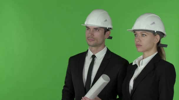 Vista frontal de la ingeniera de construcción femenina señalando de pie con el ingeniero masculino sosteniendo el plano, clave de croma — Vídeos de Stock