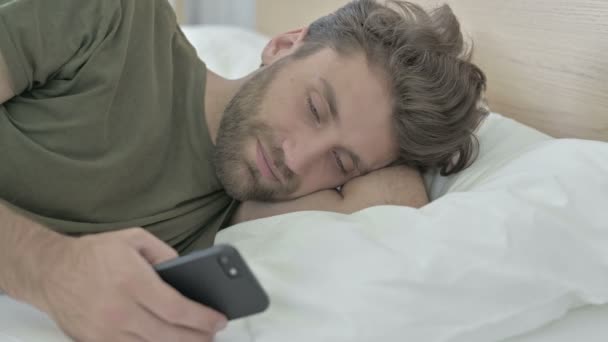 Крупный план молодого человека с помощью мобильного телефона в постели — стоковое видео