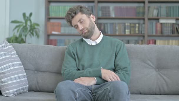 Müder junger Mann sitzt auf Sofa und macht ein kurzes Nickerchen — Stockvideo