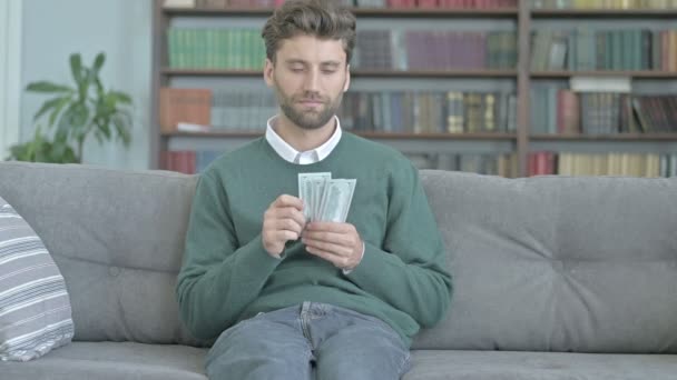 Jovem sentado no sofá e contando o dinheiro — Vídeo de Stock