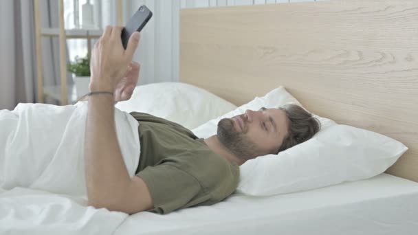 Jonge man scrollen zijn mobiele telefoon in bed — Stockvideo