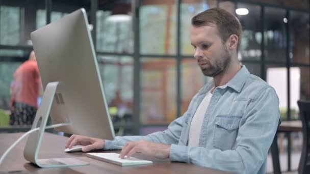 Молодий чоловік показує великі пальці вниз під час роботи на комп'ютері — стокове відео