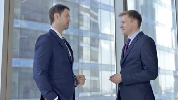 Весёлые два бизнесмена среднего возраста, которые ведут беседу против окна кабинета директоров — стоковое видео