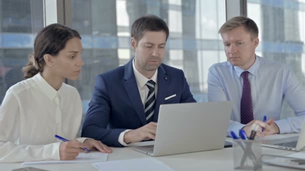 Empresario de mediana edad usando el ordenador portátil y explicando a sus asistentes en la mesa de la oficina — Vídeo de stock