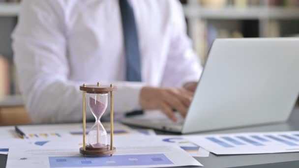 Primer plano de reloj de arena en la mesa y hombre de negocios utilizando el ordenador portátil — Vídeos de Stock