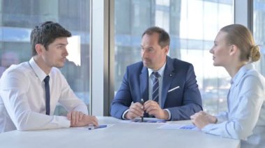 Orta yaşlı iş adamı yönetim kurulu masasında asistanlarla konuşuyor.