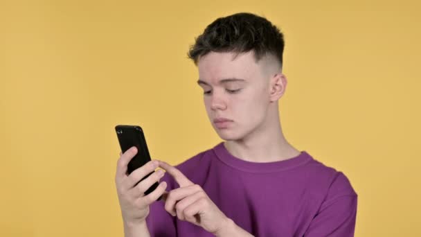 Joven hombre emocionado por el éxito mientras se utiliza el teléfono inteligente en el fondo amarillo — Vídeos de Stock
