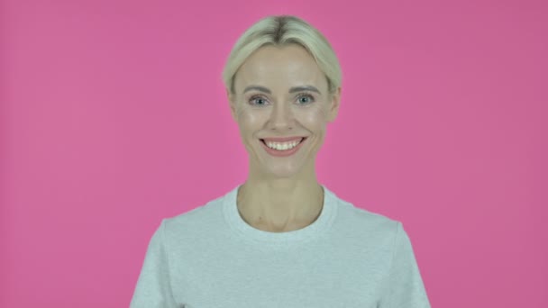 Mujer joven sonriente mirando a la cámara, fondo rosa — Vídeo de stock