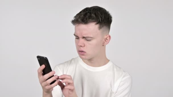 Mladý muž reaguje na ztrátu a použití chytrého telefonu na bílém pozadí — Stock video