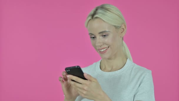 Νεαρή γυναίκα Browsing Smartphone σε ροζ φόντο — Αρχείο Βίντεο