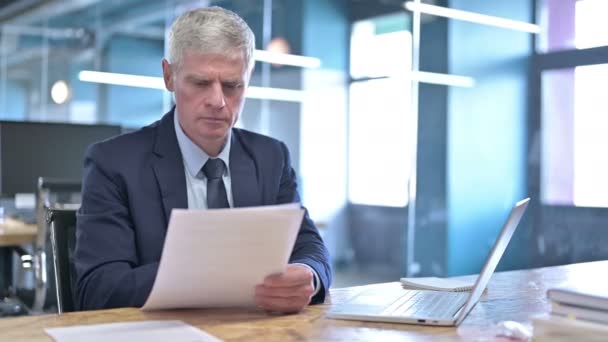 Empresario de mediana edad leyendo el documento en el escritorio de la oficina — Vídeos de Stock