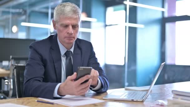 Empresario de mediana edad usando el teléfono celular en la oficina — Vídeo de stock